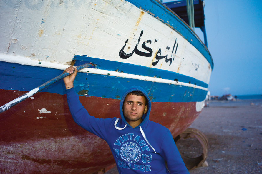 Patrick Zachmann // M. Ali Ghommidh, 19 ans, pose devant le bateau sur lequel il a embarqué, avec cent autres migrants clandestins, en direction de l’Europe. Le chalutier a failli sombrer, et ses passagers ont été sauvés par la marine tunisienne, Zarzis, avril 2011 Magnum Photos